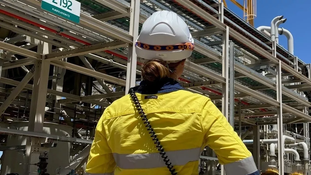 Woman in protective clothing and hardhat outside of plant.