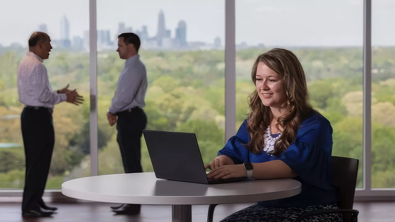Woman working on laptop at small desk.