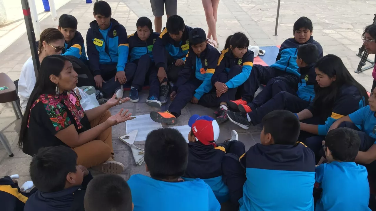 Chilean youth gathered in seated circle around adult facilitator doing an activity
