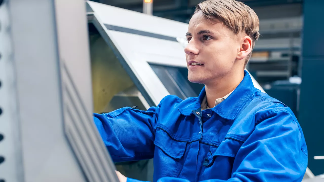 Young male worker programming lathe machine in factory.
