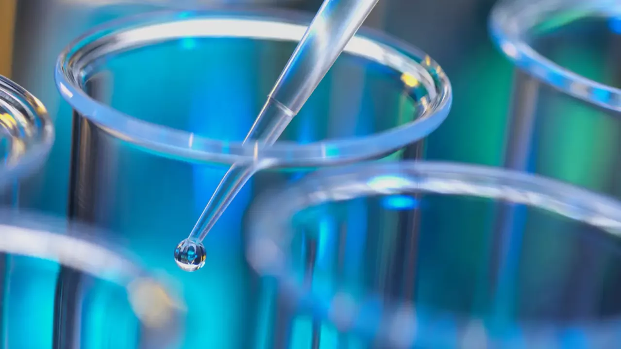 A pipette dispensing a drop of liquid into one of several test tubes in a scientific laboratory setting, highlighting precision and experimentation.