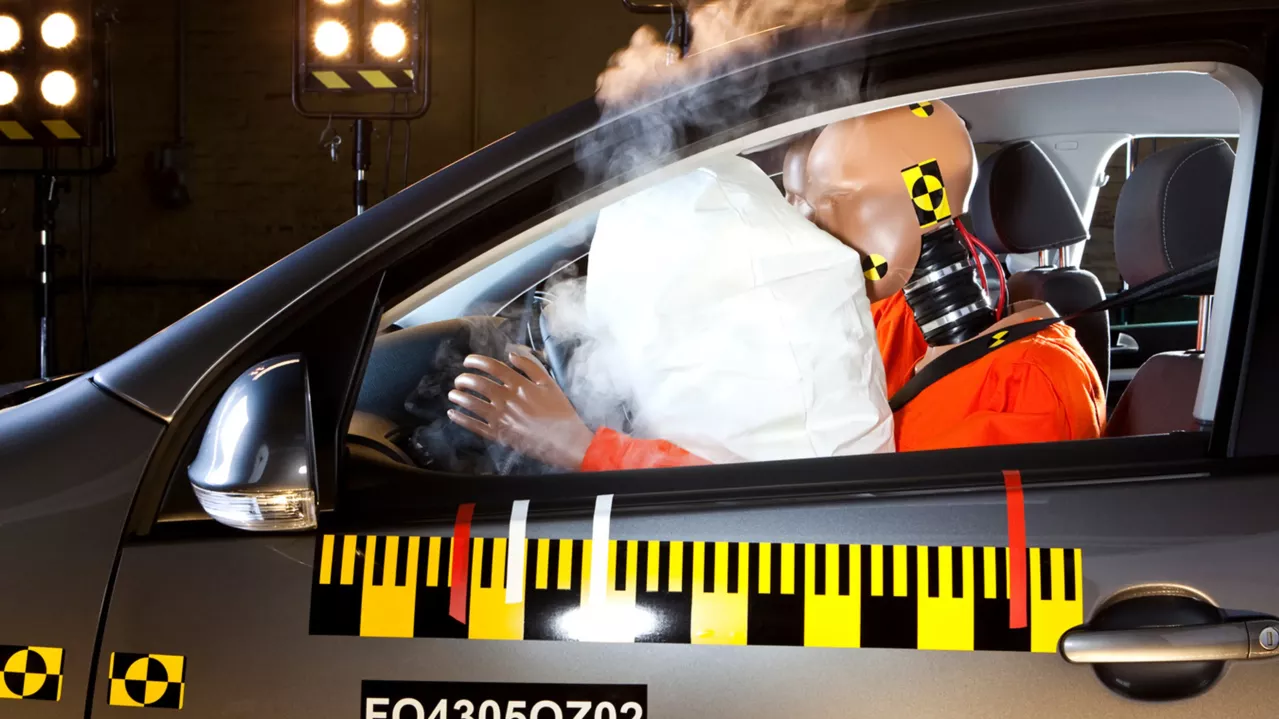 A crash test dummy inside a car experiencing airbag deployment during a safety test in a laboratory setting.