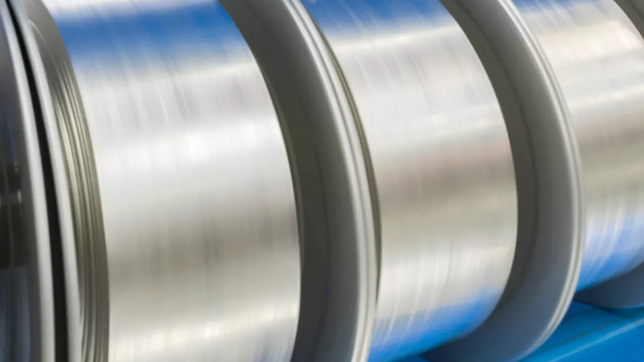 Close-up view of large, shiny aluminum coils in a factory setting, showcasing the metallic surfaces with blurred motion effect.