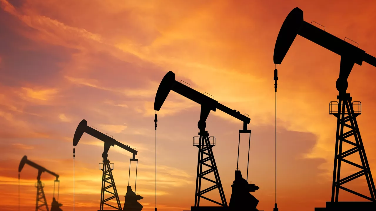 Silhouettes of multiple oil pump jacks against a vibrant orange sunset sky, symbolizing energy extraction and industrial activity.