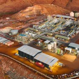 Aerial view of a large industrial complex set against a rugged, arid landscape. The facility features multiple buildings, structures, and machinery, with roads connecting different sections. Various equipment, vehicles, and storage tanks are visible throughout the site.