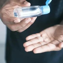 A close up of a person dispensing hand sanitizer from a clear bottle into their palm, emphasizing hygiene and health safety.