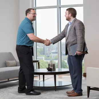 Two men shaking hands in small lobby. 