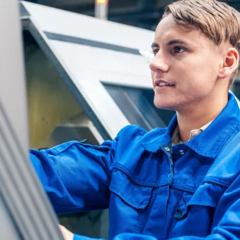 Young male worker programming lathe machine in factory.