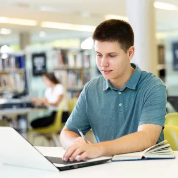 Young man on laptop in library.