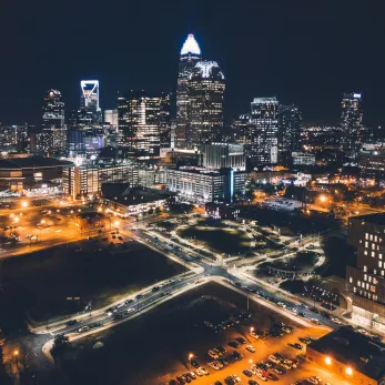 Aerial night view of a bustling city with illuminated skyscrapers, roads, and a few cars, showcasing a vibrant urban landscape.