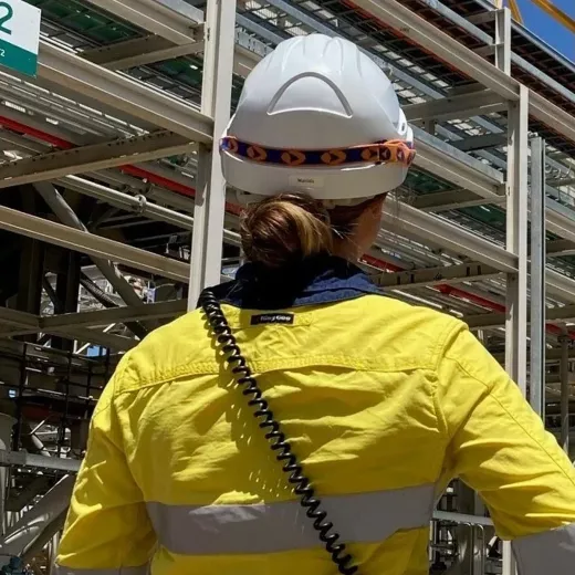 Woman in protective clothing and hardhat outside of plant.