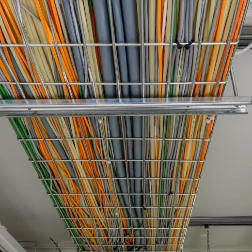 Wire baskets hanging from the ceiling, filled with numerous colored internet cables, viewed from below.