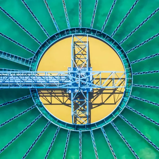 Aerial view of water treatment plant with with symmetric blue steel walkways centered on a bright yellow circular platform, creating a geometric pattern against a green backdrop.