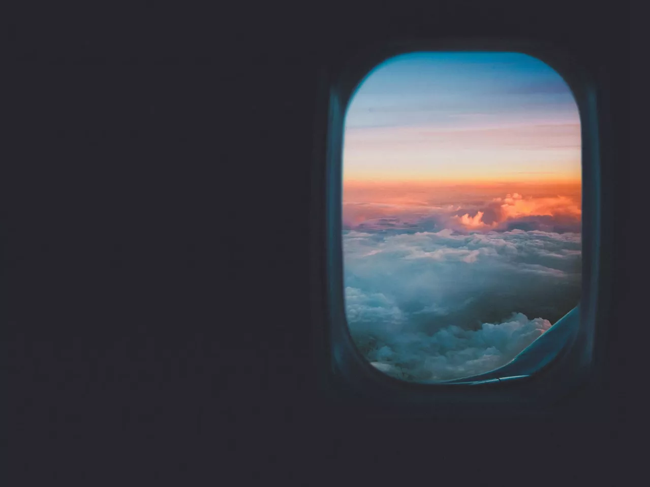 View from an airplane window showing a vibrant sunrise with orange and pink hues over a cloudy sky, creating a serene and picturesque scene.